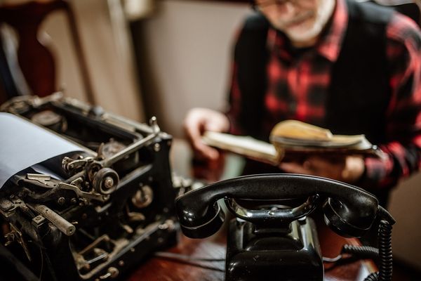 An old typewriter and vintage telephone on a desk in a cosy room
