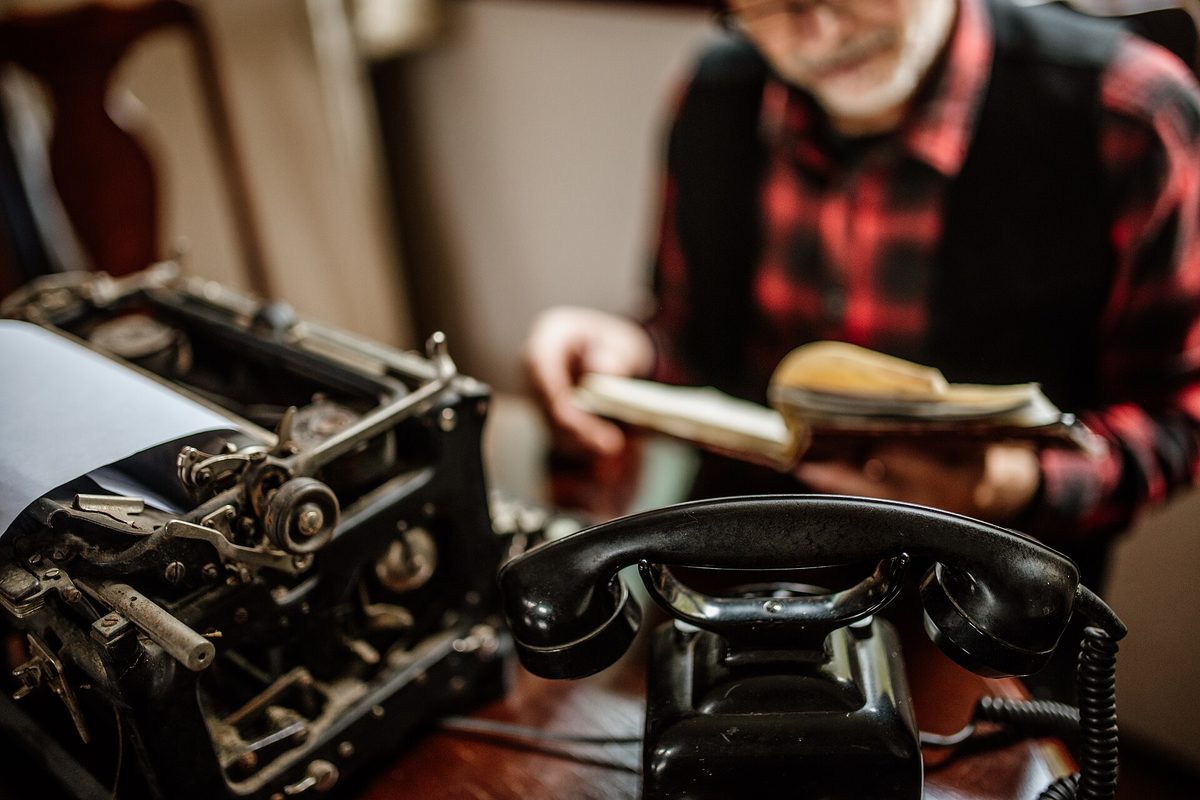 An old typewriter and vintage telephone on a desk in a cosy room